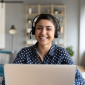 A smiling lady with headphones behind a laptop