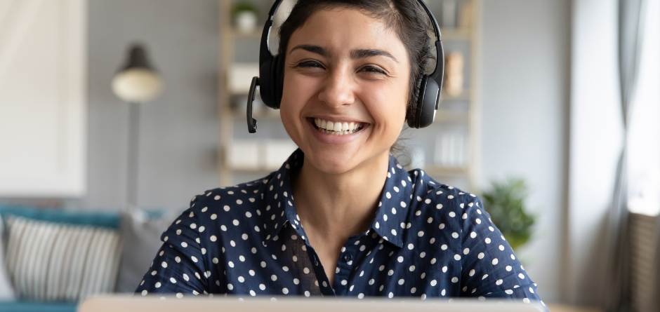 A smiling lady with headphones behind a laptop