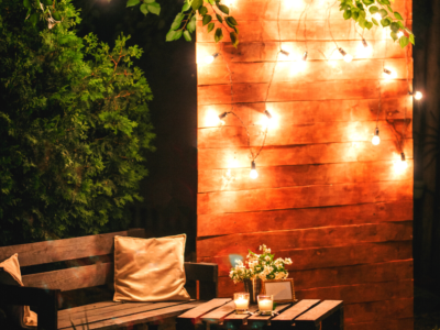 A cosy outdoor area that includes a bench with cushions, a small table with candles and a screen with fairy lights