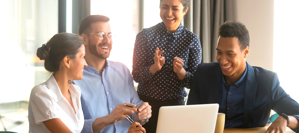 Four happy people behind a laptop looking relieved