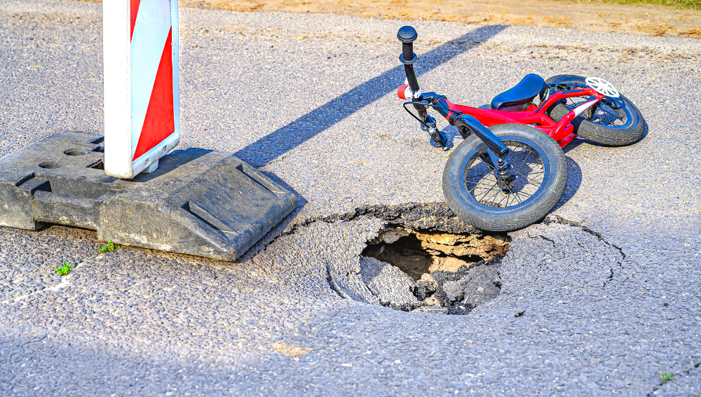 A push bike lying next to a pothole in the road