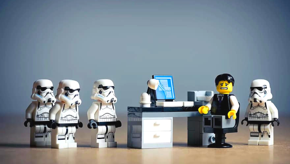Star wars lego characters surrounding a nervous looking character behind a desk